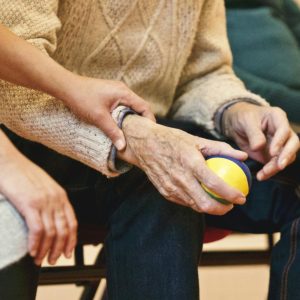 An elderly person receives support from a caregiver, holding hands indoors, showcasing compassion.