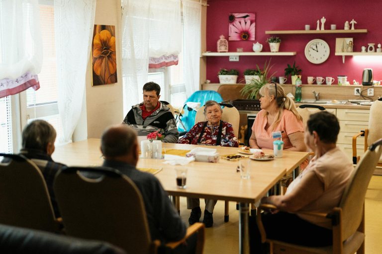 Seniors enjoying a meal in a nursing home dining room with caregivers in Karviná, Czechia.